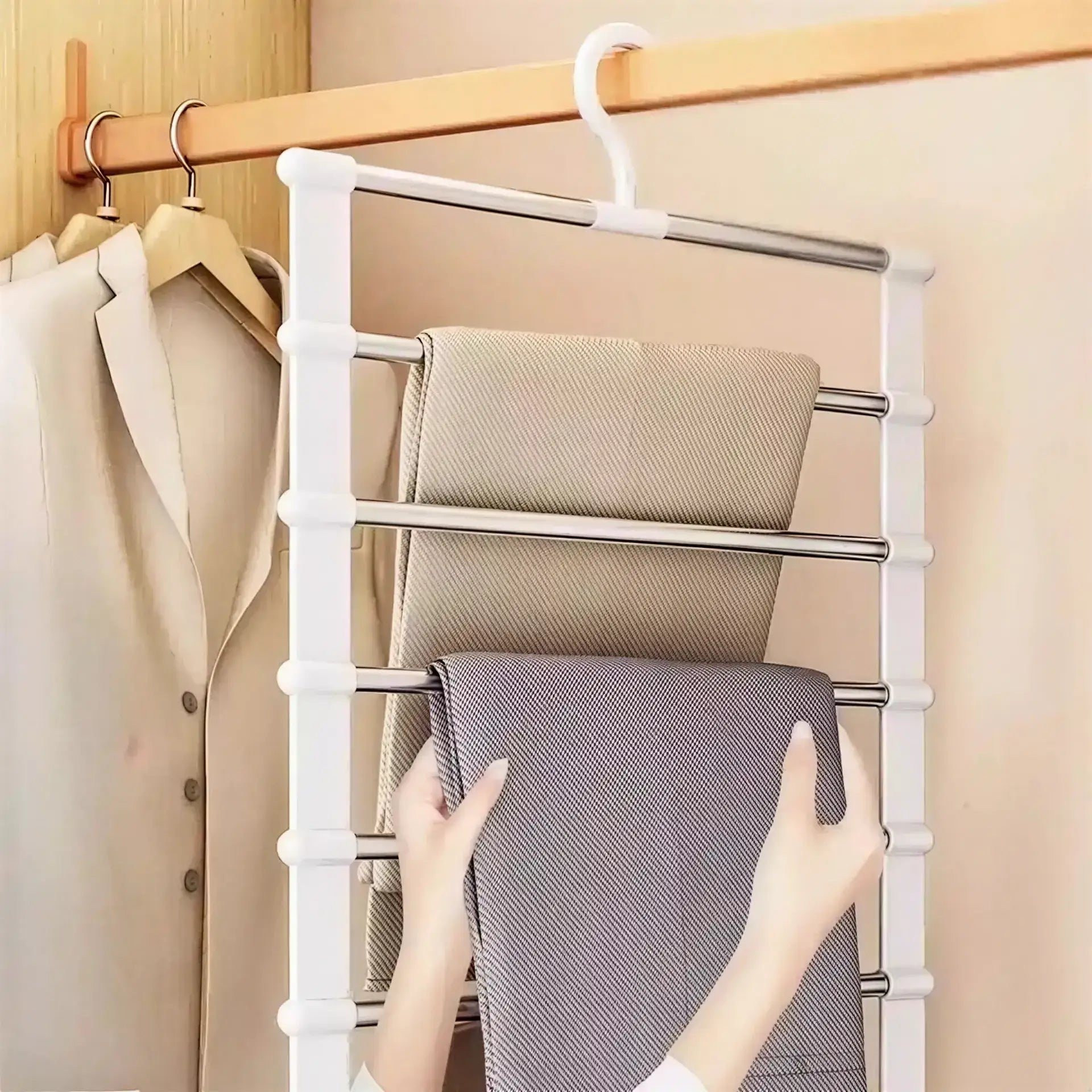 White plastic and metal multi-tier pants hanger with five horizontal rods holding folded fabric in a closet.