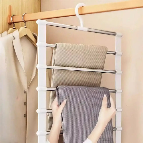 White plastic and metal multi-tier pants hanger with five horizontal rods holding folded fabric in a closet.