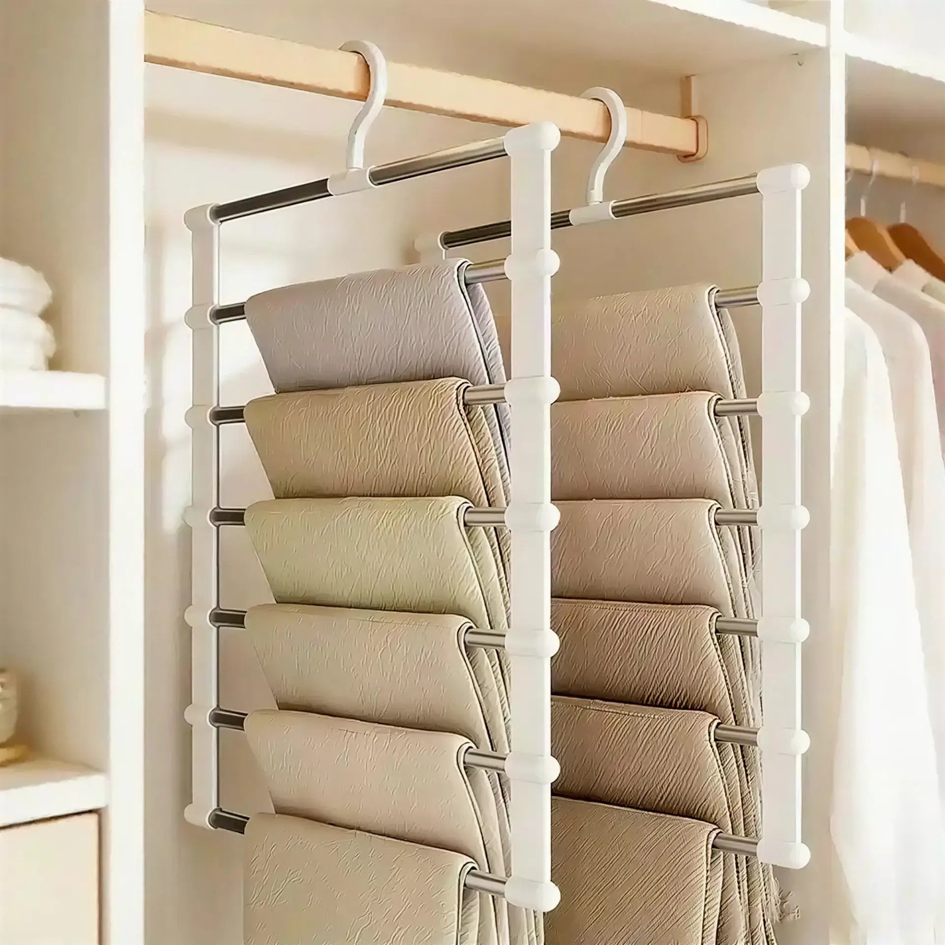 Two white and metal multi-tier pants hangers holding several pairs of folded fabric trousers in a closet.